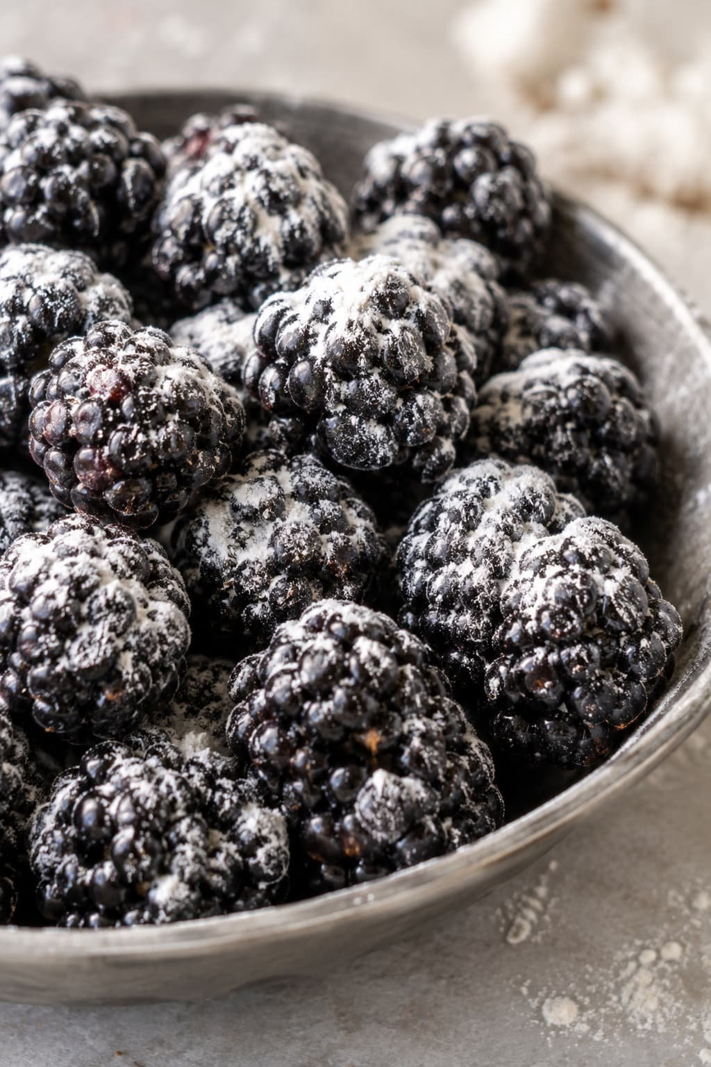 Close-up of fresh blackberries lightly tossed in dry flour to prevent them from sinking during the baking process.