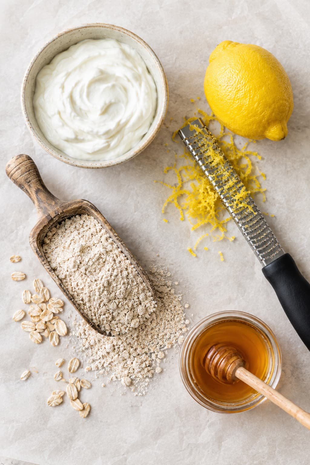 Top-down view of healthy baking staples including Greek yogurt, whole-grain flour, honey, and fresh lemons.