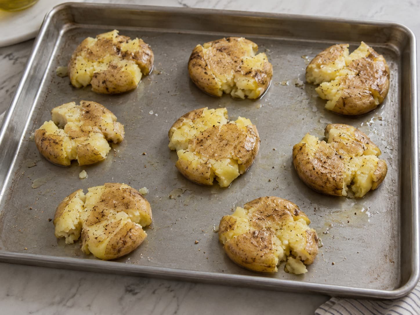 Smashed potatoes spaced apart on a baking tray with exposed cracked surfaces