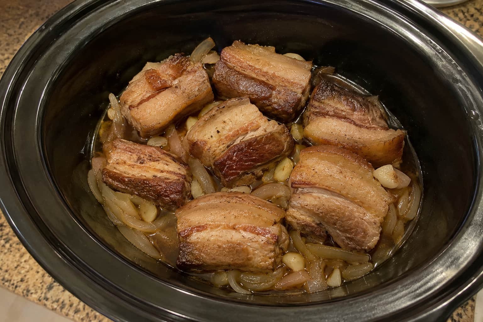 Pork belly with aromatics and a small amount of cooking liquid in a slow cooker