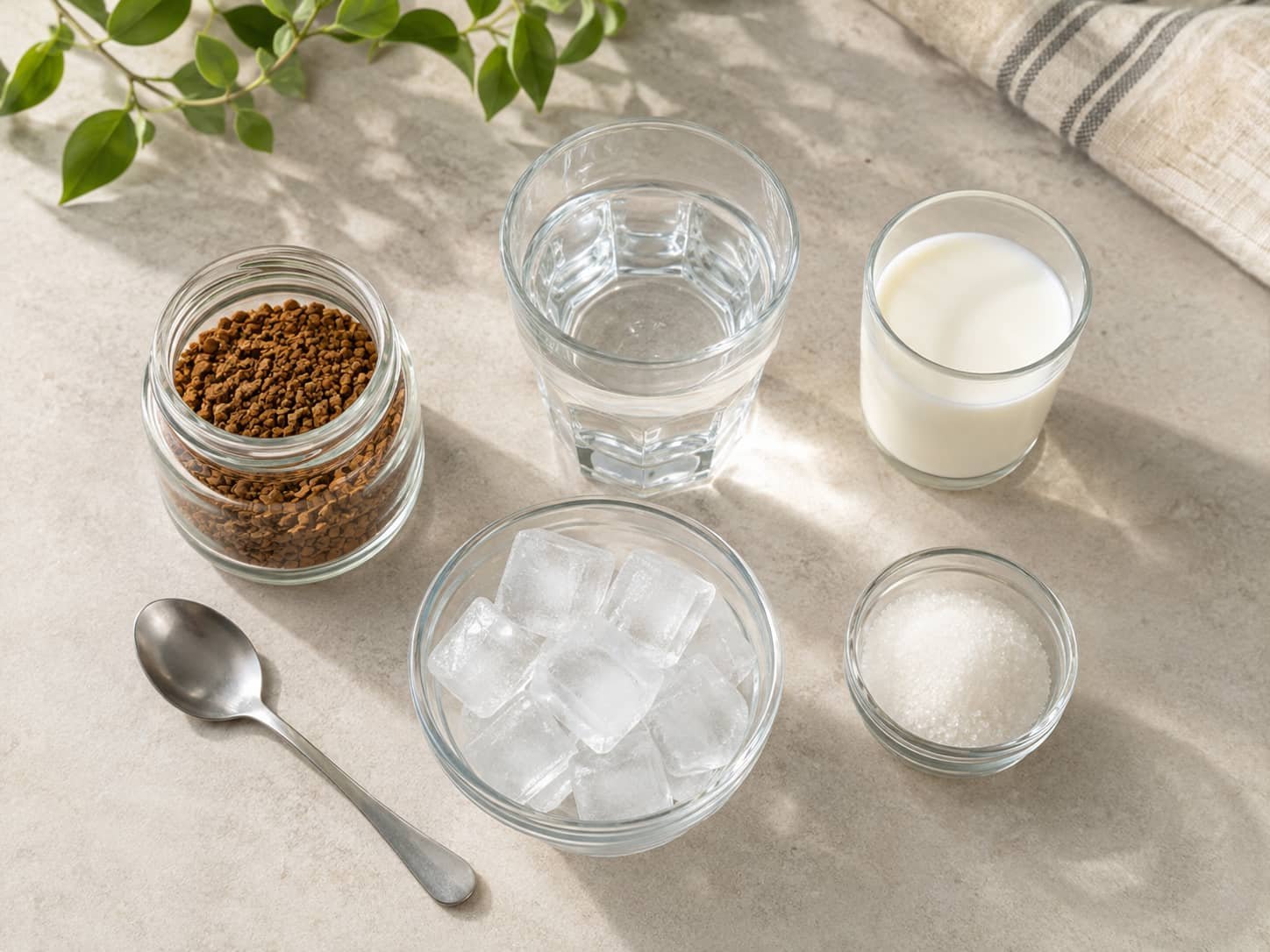 Instant coffee granules, cold water, milk, ice, and sugar arranged for making iced coffee