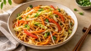 Chinese-style stir-fried wheat noodles with cabbage, carrots, bell peppers, and green onions in a ceramic bowl.